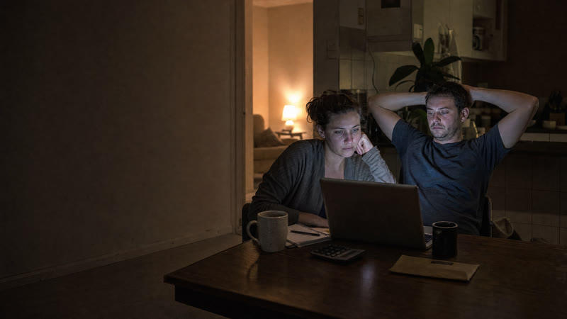 A couple working at a kitchen table late at night, the laptop screen turned away