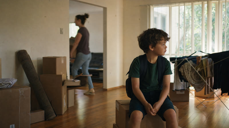 A child in a school backpack waiting on a packing box in a half-emptied living room