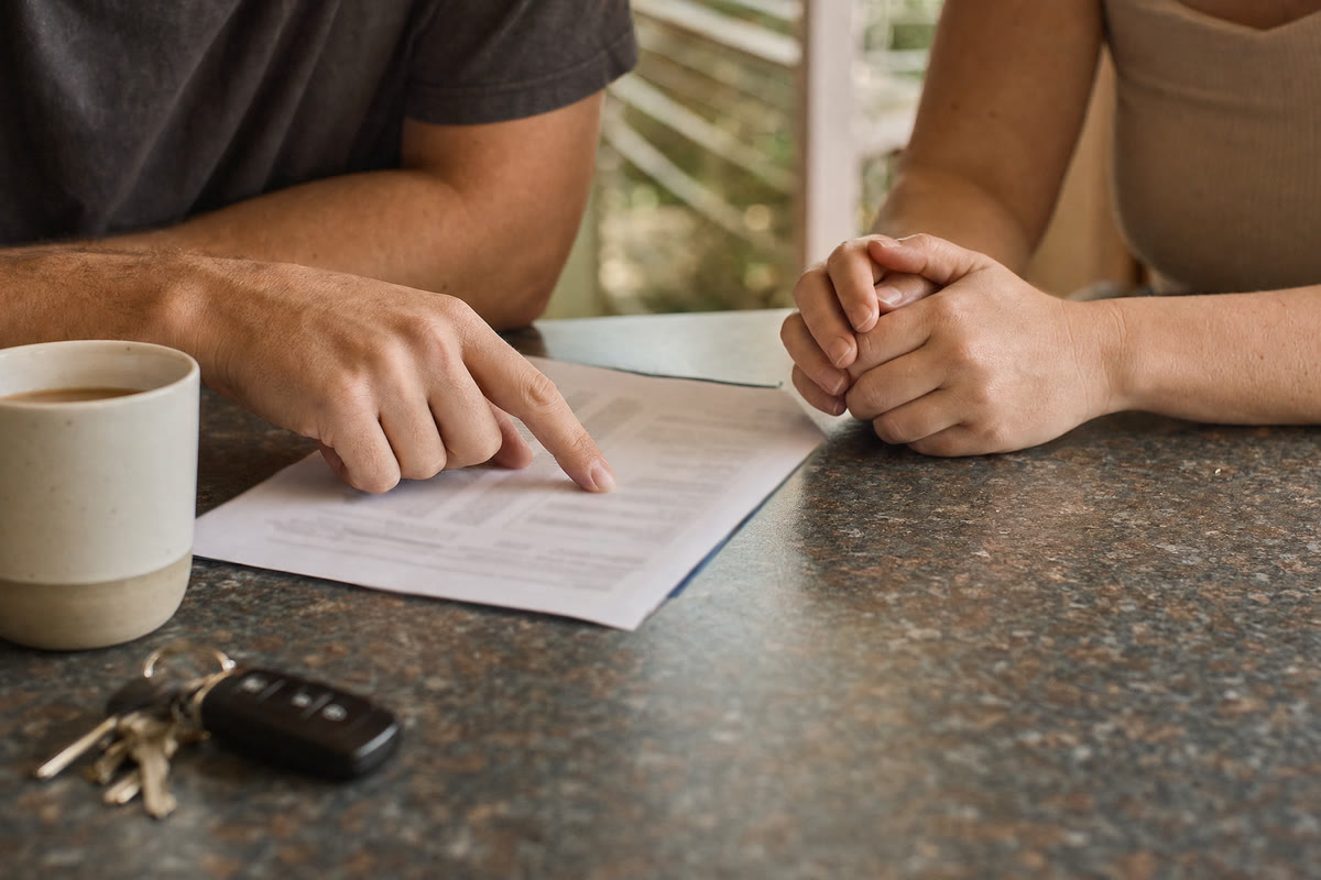 Two pairs of hands over a paper form on a kitchen bench, one tracing a line down the page